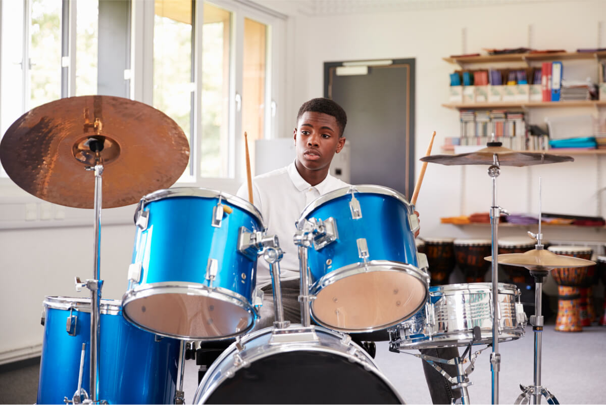 male-teenage-pupil-playing-drums-in-music-lesson-2022-03-30-20-23-47-utc